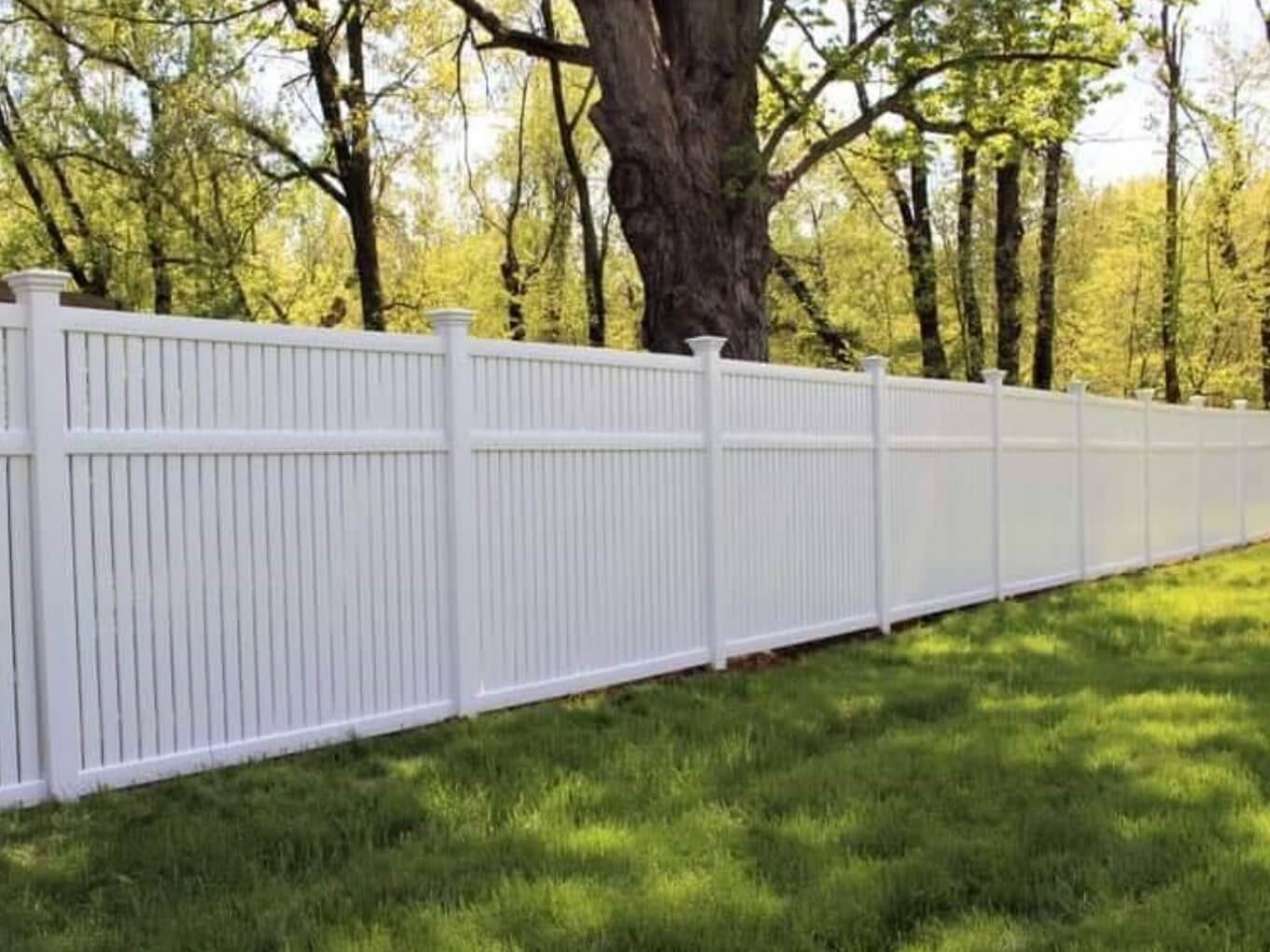 Solid white vinyl privacy fence in a grassy backyard with trees behind it