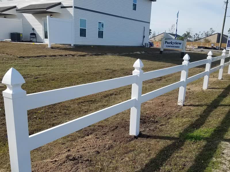 White two-rail ranch-style vinyl fence with pyramid post caps at a new construction site
