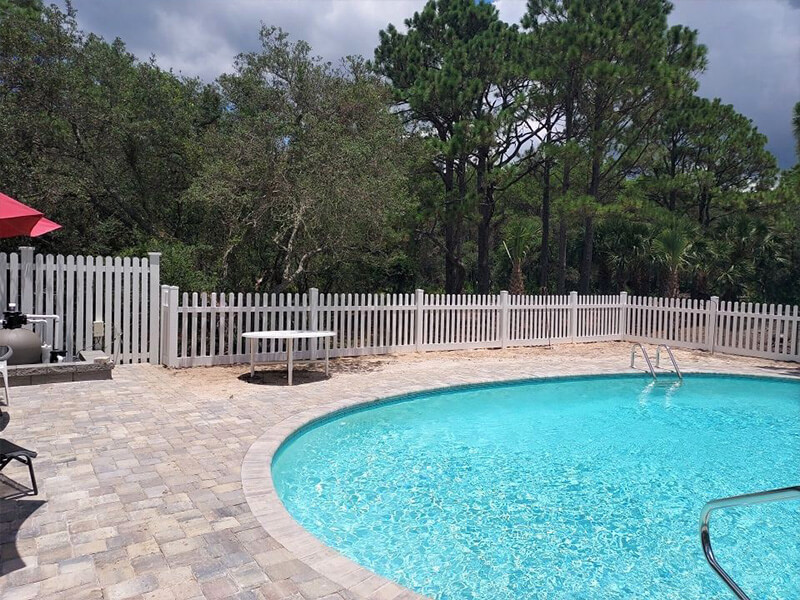 White vinyl picket pool safety fence around a blue swimming pool and paver deck