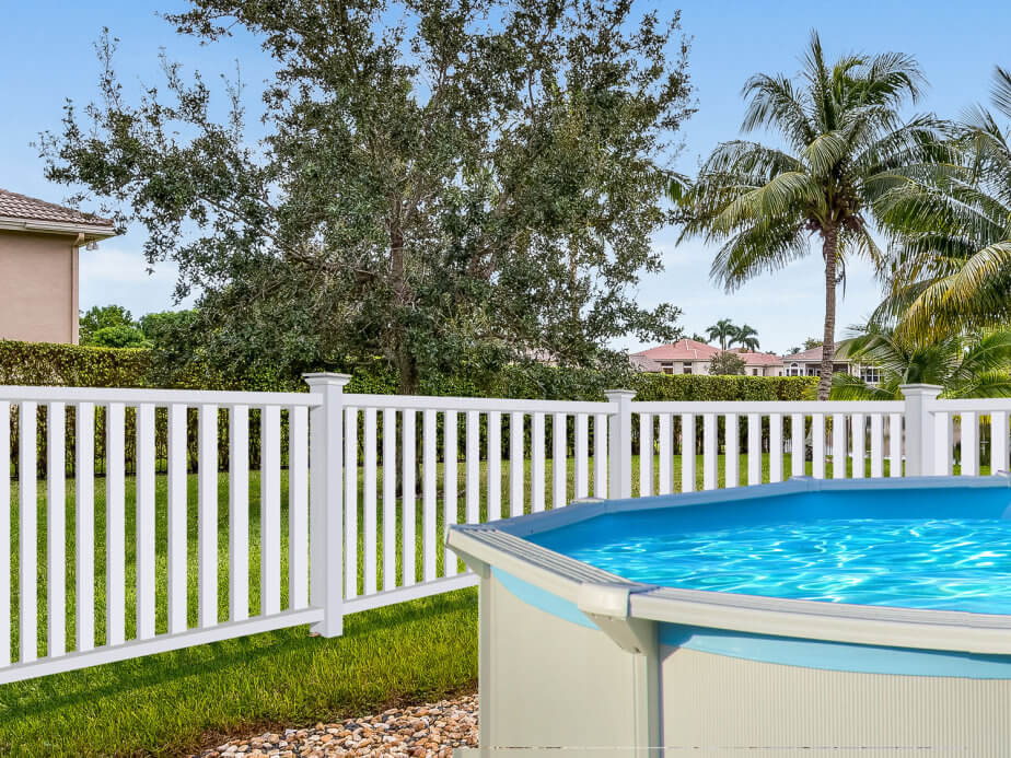 White vinyl picket fence around a wooden deck and above-ground pool in a backyard
