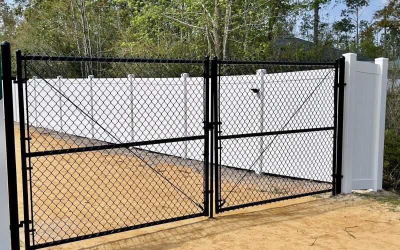 Black chain link double-drive gate set into a white vinyl privacy fence