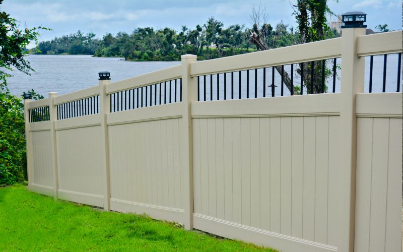 White vinyl privacy fence with black aluminum spindle topper on a grassy bank overlooking water