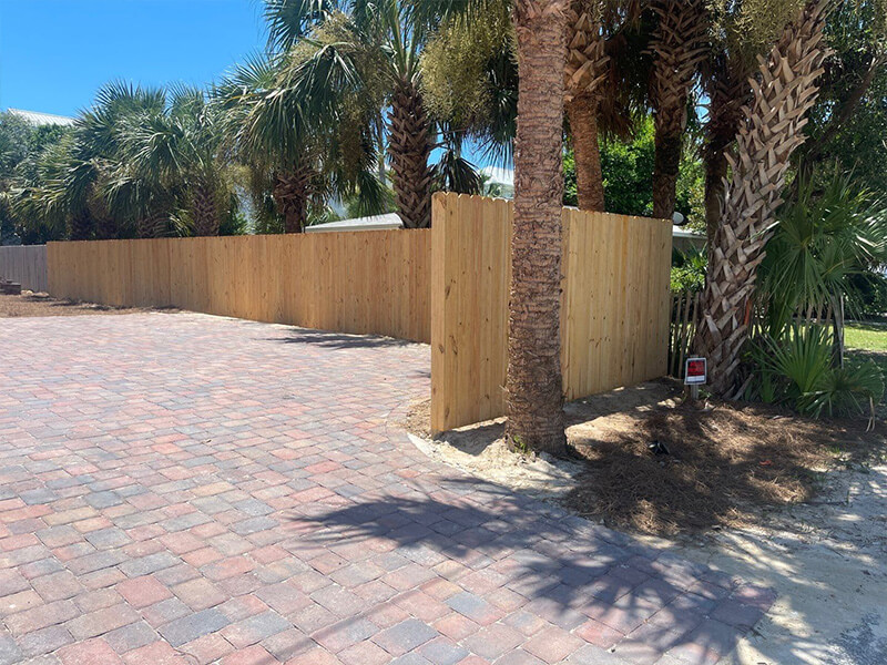 Vertical wood privacy fence beside herringbone brick pavers with palm trees behind