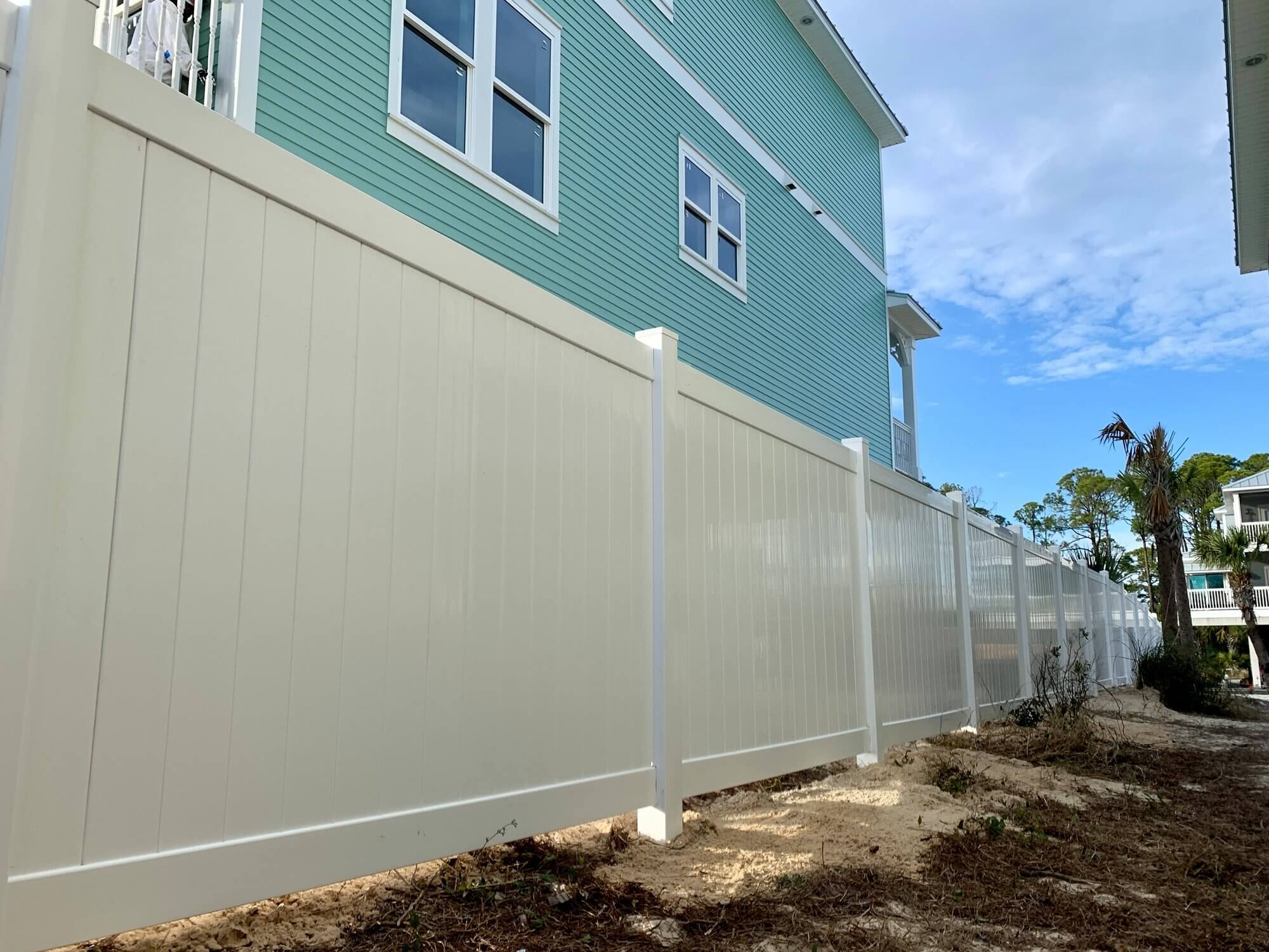 Tall white vinyl privacy fence beside a light-blue two-story home