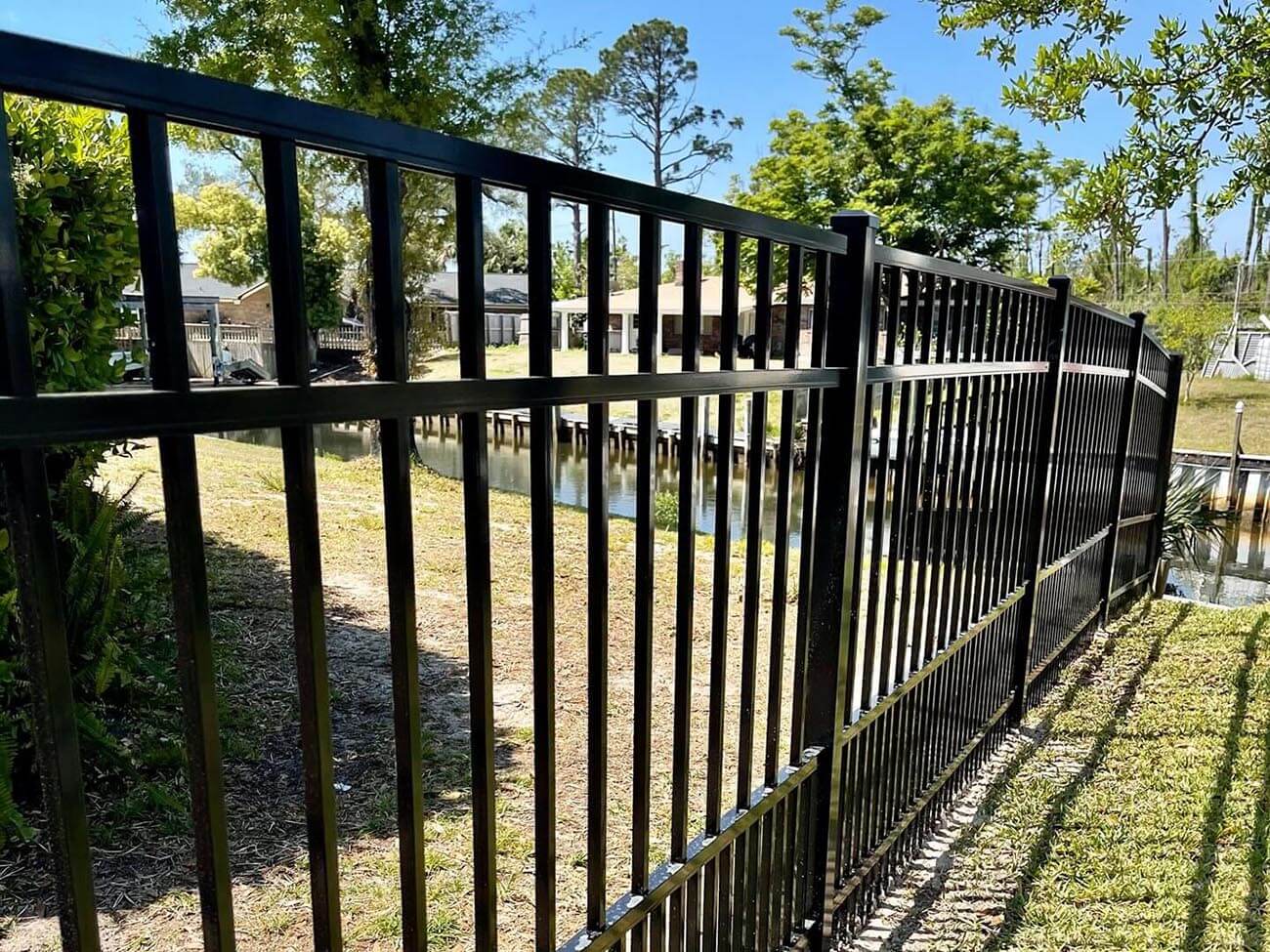 Black aluminum picket fence with a bay or canal and trees visible through the pickets