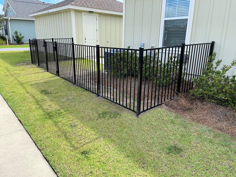 Black aluminum picket fence enclosing a small lawn beside a light-colored house