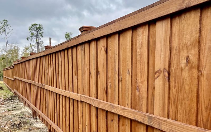 Long reddish-brown stained wood privacy fence following gently sloping ground