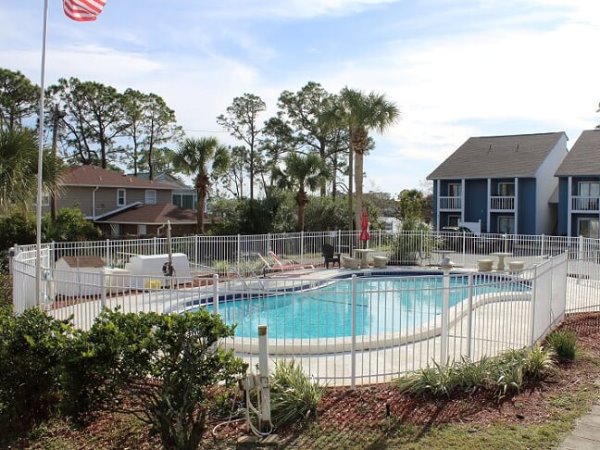 White safety fence around a blue swimming pool with palm trees and two-story buildings behind