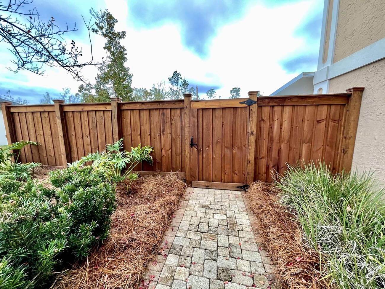 Dark-stained wood privacy fence and matching gate with a brick paver walkway