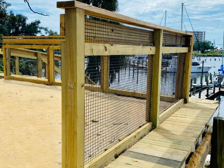 Wire-and-wood fence along a waterfront walkway near a marina