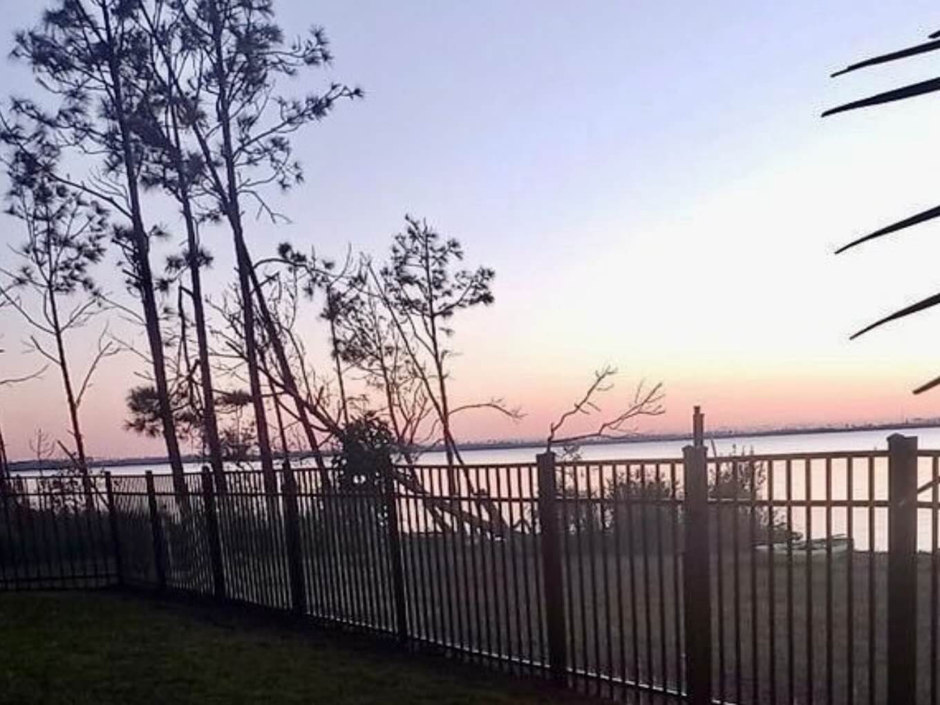 Black aluminum picket fence along a grassy yard beside a bay at sunset