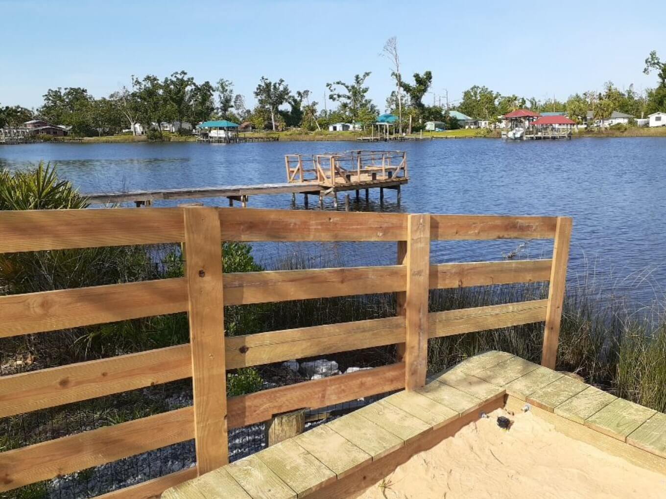 Natural wood three-rail fence at the water's edge beside a small wooden dock