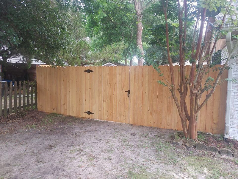 Wood privacy fence with a wide double gate in a shaded backyard with mature trees