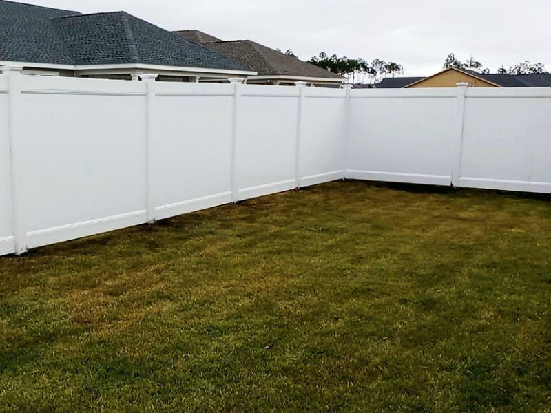 White vinyl privacy fence forming a corner around a freshly sodded backyard