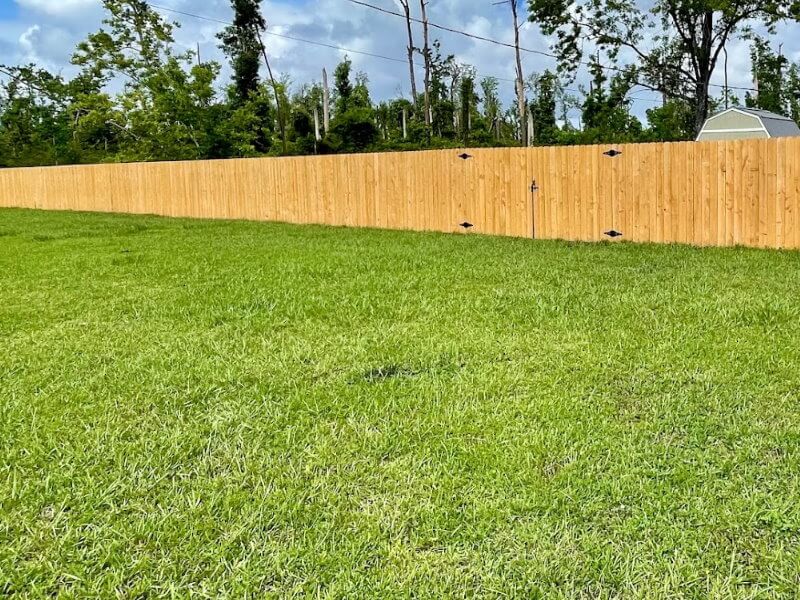 Long horizontal-plank wood privacy fence bordering a wide open lawn