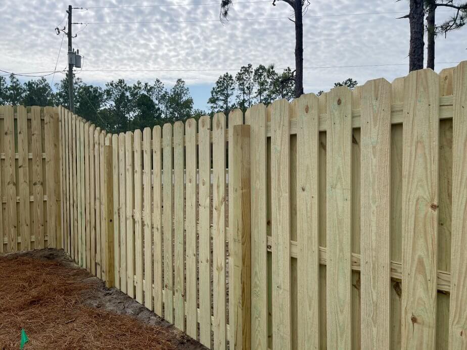 Vertical shadowbox wood fence following a slight slope against a backdrop of trees