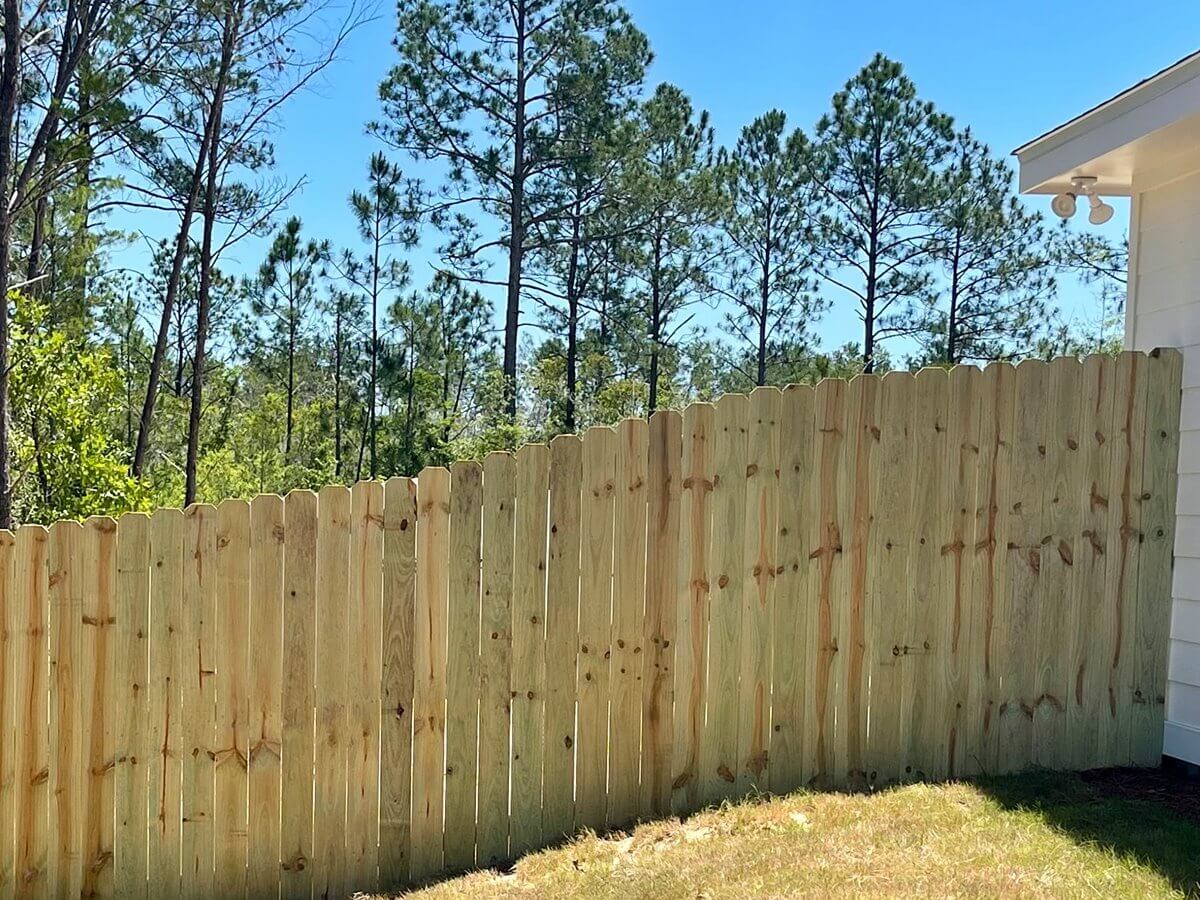 Stockade wood privacy fence with pointed tops along an uneven grassy grade
