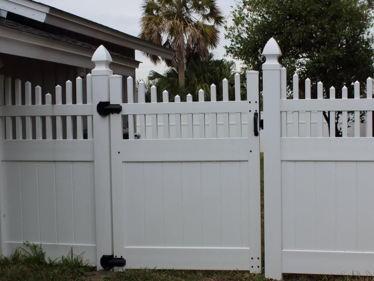 Close view of a white vinyl picket fence and gate with pointed post caps and black latches, a Bay County installation