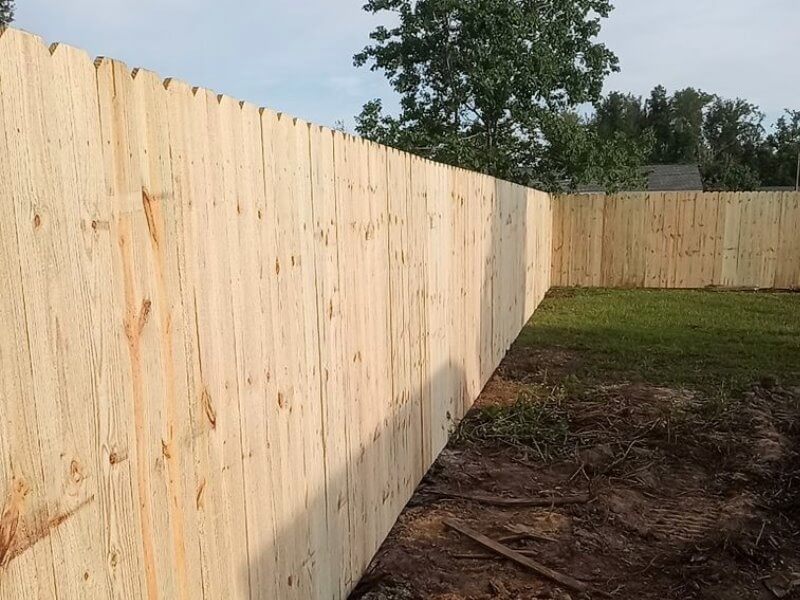 Tall new wood privacy fence with vertical pickets turning a corner in a yard