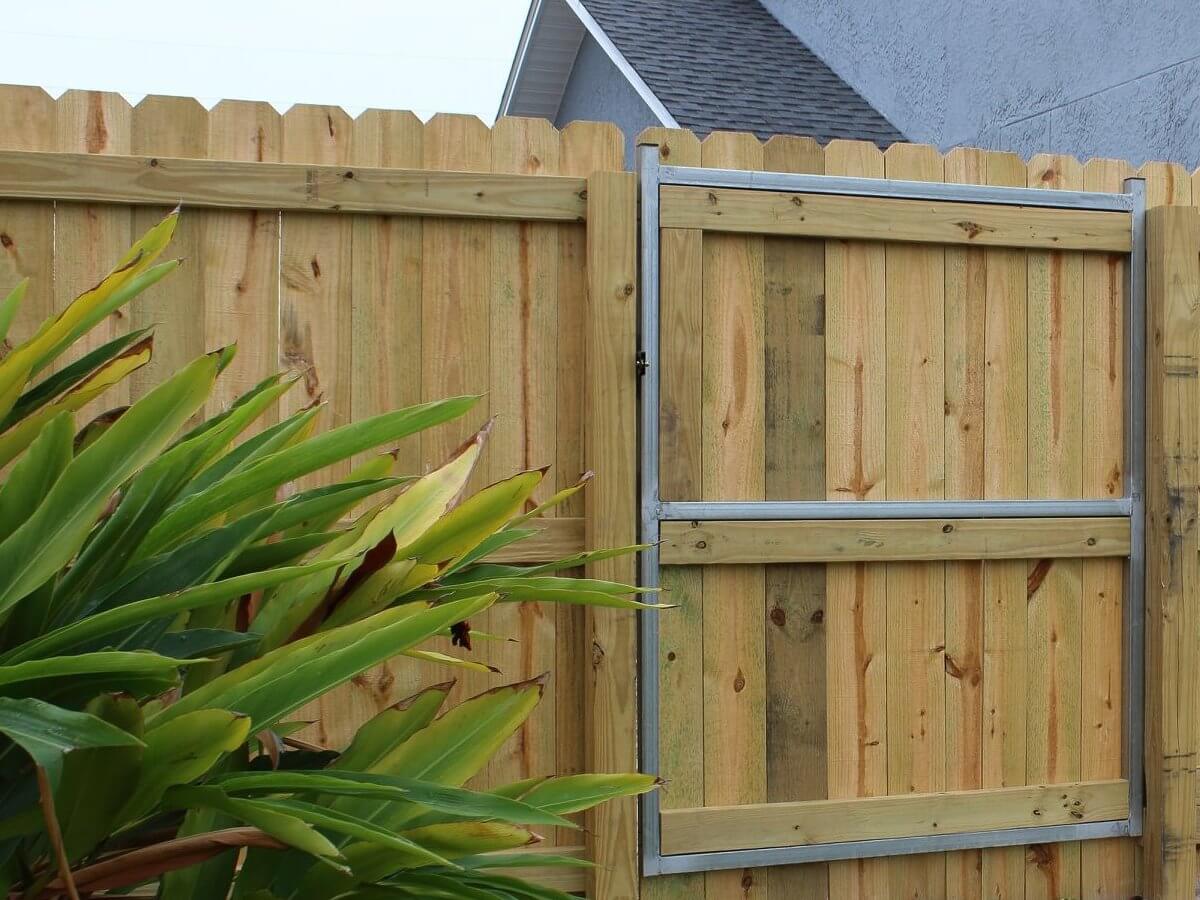 Wood privacy gate showing the metal frame reinforcement inside, with tropical plants in front, a Bay County installation